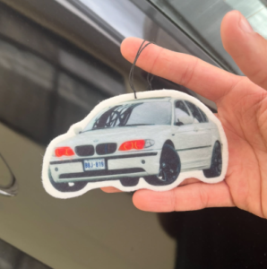 Ambientador con forma de BMW Serie 3 blanco sostenido en la mano